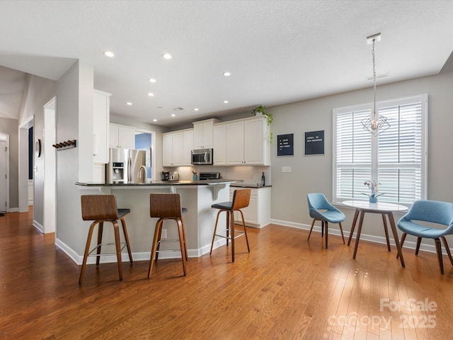 kitchen with a kitchen breakfast bar, white cabinets, pendant lighting, and appliances with stainless steel finishes