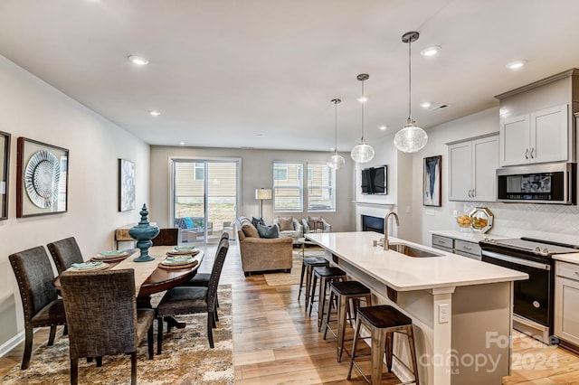 kitchen featuring sink, hanging light fixtures, stainless steel appliances, an island with sink, and light wood-type flooring