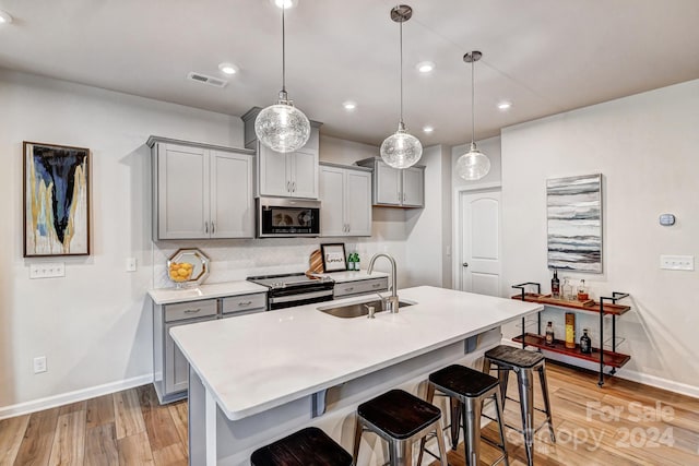 kitchen with gray cabinetry, sink, light hardwood / wood-style flooring, pendant lighting, and appliances with stainless steel finishes