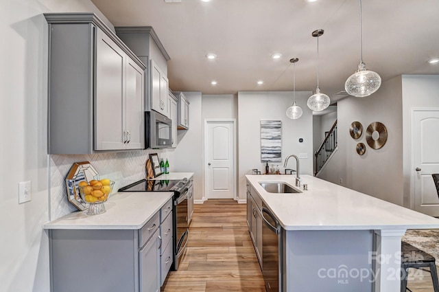 kitchen with sink, decorative light fixtures, a kitchen island with sink, appliances with stainless steel finishes, and light wood-type flooring