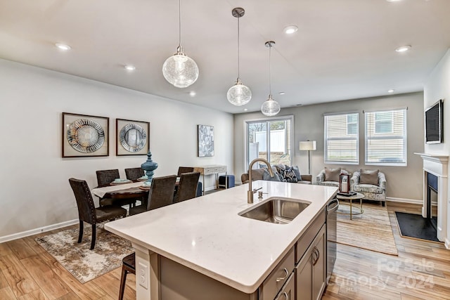 kitchen with a kitchen island with sink, sink, pendant lighting, light hardwood / wood-style flooring, and dishwasher