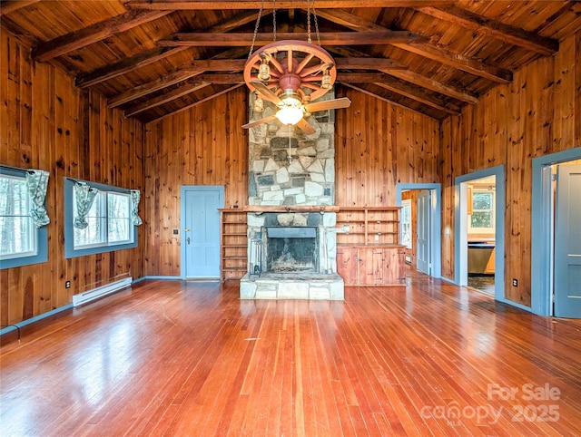 unfurnished living room with a baseboard heating unit, a stone fireplace, wood walls, and wood-type flooring