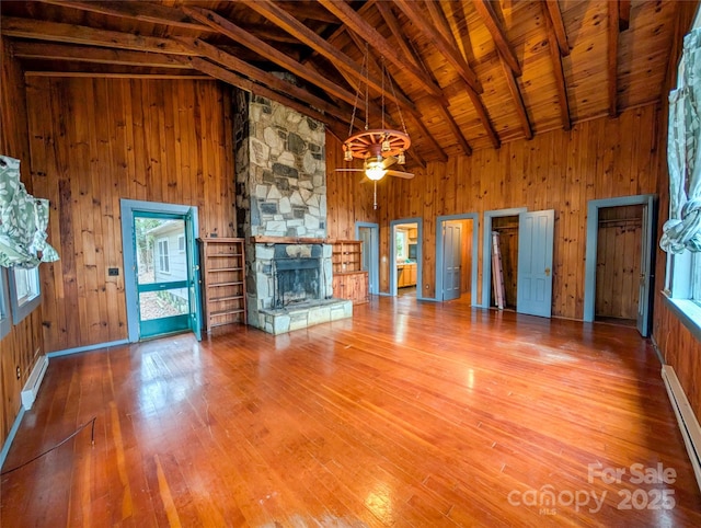 unfurnished living room with beam ceiling, a stone fireplace, wood walls, and wood finished floors