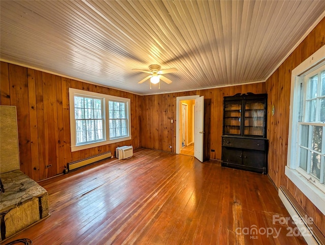 unfurnished living room with a healthy amount of sunlight, a baseboard heating unit, and hardwood / wood-style flooring