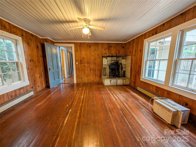 unfurnished living room featuring wooden walls, a stone fireplace, baseboard heating, a ceiling fan, and wood-type flooring