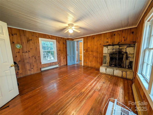 unfurnished living room featuring hardwood / wood-style floors, wooden walls, a stone fireplace, baseboard heating, and ceiling fan