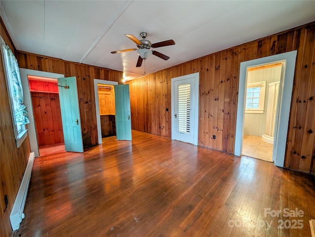 unfurnished bedroom featuring multiple closets, baseboard heating, and hardwood / wood-style flooring