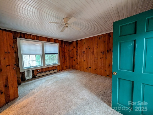 spare room with wooden walls, carpet flooring, a baseboard heating unit, and a ceiling fan