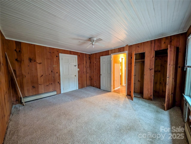 unfurnished bedroom with a baseboard heating unit, wooden walls, carpet flooring, and ceiling fan