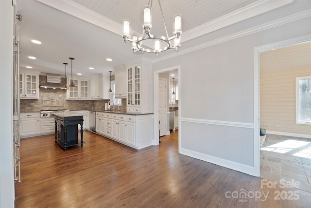 kitchen featuring appliances with stainless steel finishes, white cabinetry, hanging light fixtures, a center island, and wall chimney range hood