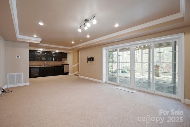 unfurnished living room featuring ornamental molding, a tray ceiling, carpet, and wet bar