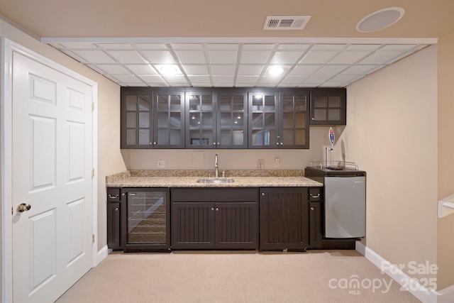 bar featuring sink, beverage cooler, dark brown cabinetry, light stone countertops, and light carpet