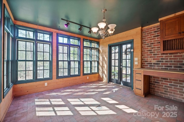 unfurnished dining area with a chandelier, wooden walls, and french doors