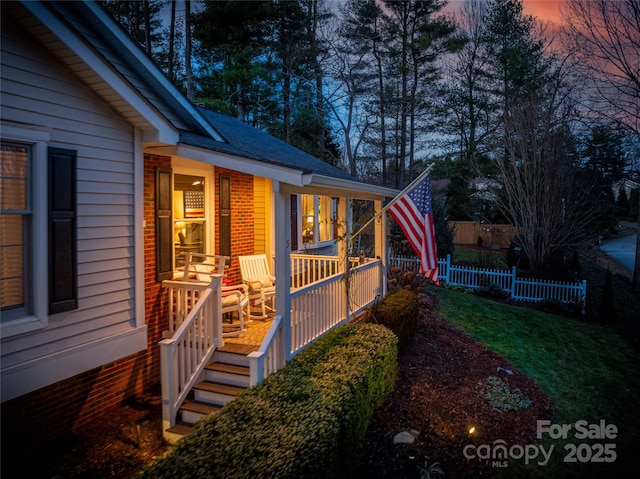 property exterior at dusk featuring a lawn and a porch