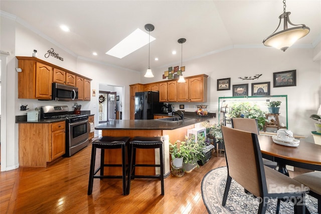 kitchen with appliances with stainless steel finishes, a breakfast bar, lofted ceiling with skylight, sink, and decorative light fixtures