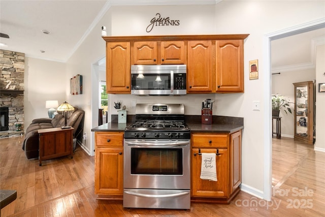 kitchen featuring ornamental molding, a fireplace, light hardwood / wood-style floors, and appliances with stainless steel finishes