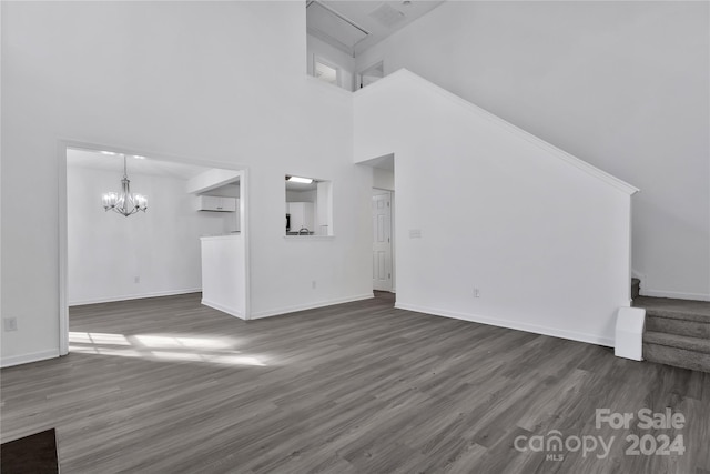 unfurnished living room featuring a towering ceiling, an inviting chandelier, and dark wood-type flooring