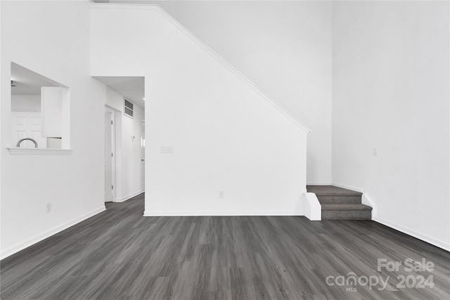 unfurnished living room featuring a towering ceiling and dark wood-type flooring