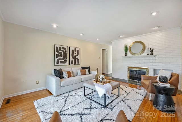 living room with light wood-type flooring, a brick fireplace, and ornamental molding