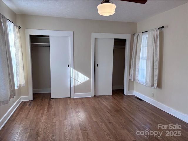 unfurnished bedroom featuring ceiling fan, dark wood-type flooring, two closets, and a textured ceiling