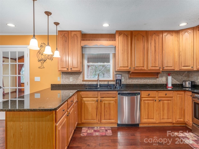 kitchen featuring dark stone counters, stainless steel appliances, dark wood-type flooring, sink, and pendant lighting