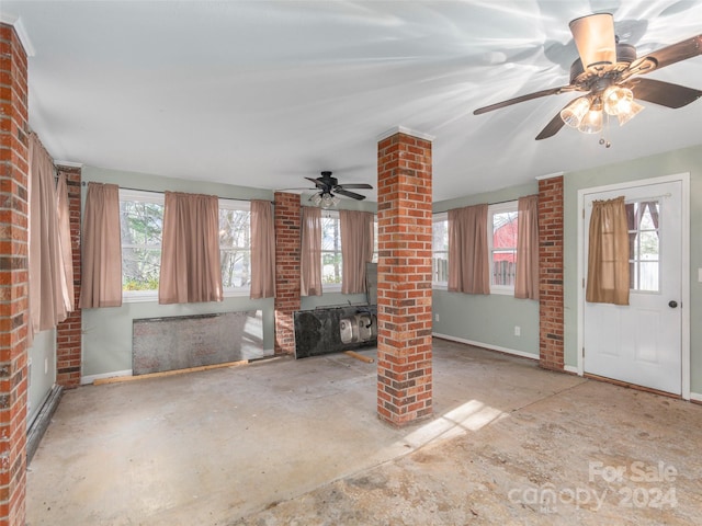 unfurnished living room with ceiling fan, brick wall, a wealth of natural light, and decorative columns