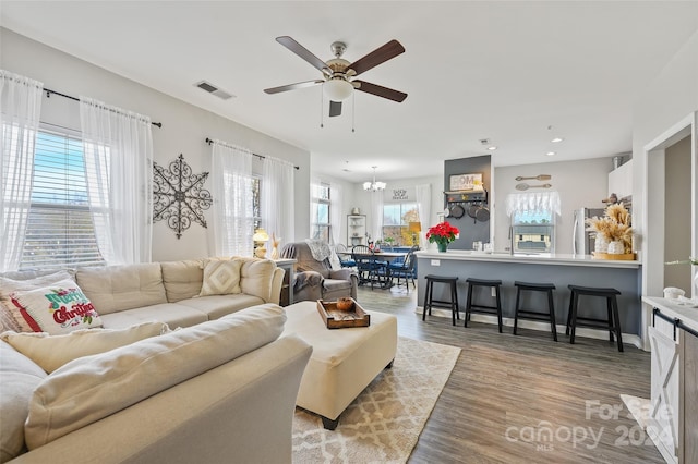 living room with ceiling fan with notable chandelier, light hardwood / wood-style floors, and a healthy amount of sunlight