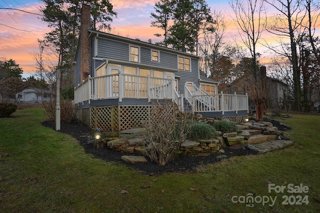 back house at dusk with a lawn and a wooden deck