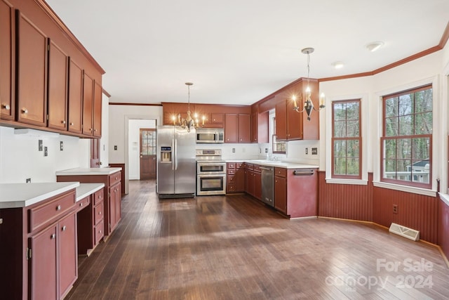 kitchen featuring appliances with stainless steel finishes, dark wood-type flooring, crown molding, pendant lighting, and a notable chandelier