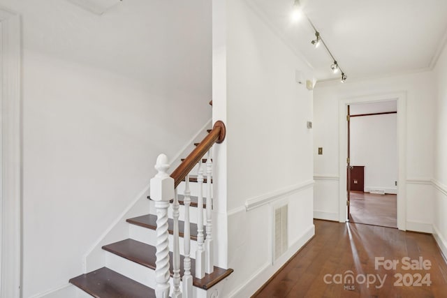 stairs featuring wood-type flooring, track lighting, and ornamental molding