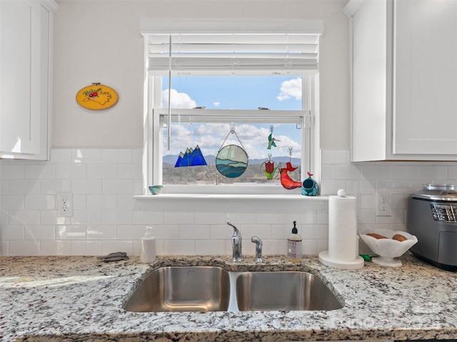 kitchen featuring light stone counters, sink, and white cabinets