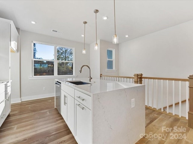 kitchen with light stone counters, sink, white cabinetry, and an island with sink