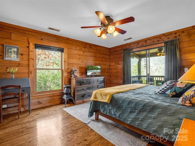 bedroom featuring ceiling fan, wood walls, wood-type flooring, and access to outside