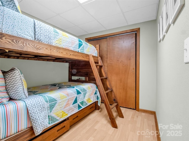 bedroom with a drop ceiling, light wood-type flooring, and a closet