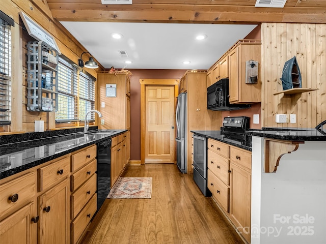 kitchen with a breakfast bar area, a sink, wood finished floors, black appliances, and dark stone counters