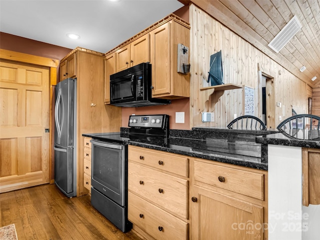 kitchen with stainless steel appliances, dark stone counters, vaulted ceiling, dark wood-style floors, and light brown cabinets