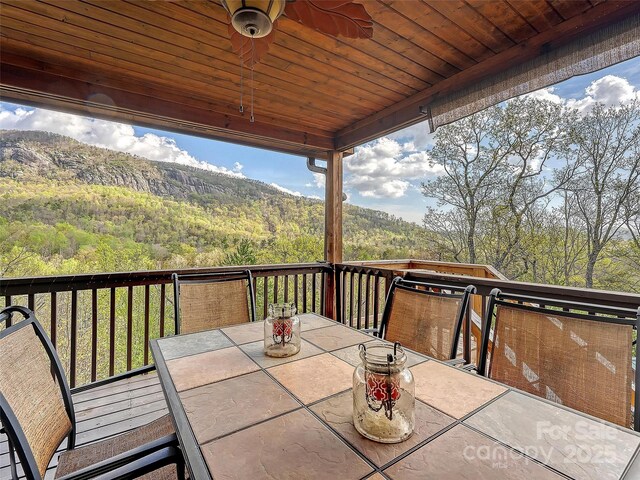 wooden terrace featuring outdoor dining area and a view of trees