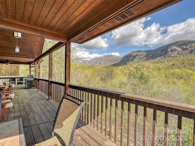wooden terrace with a mountain view, a grill, and a forest view