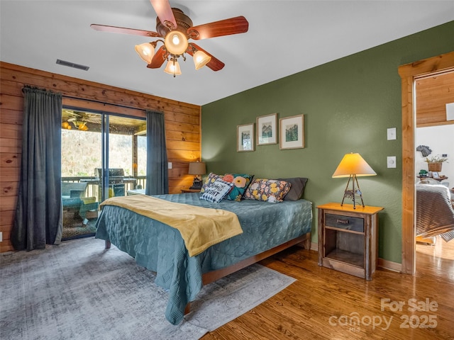 bedroom featuring access to outside, wood finished floors, ceiling fan, wooden walls, and baseboards