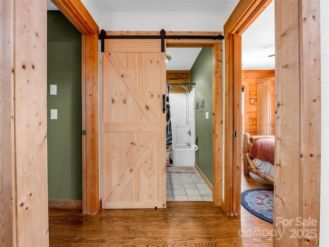 hallway featuring a barn door, wood finished floors, and baseboards