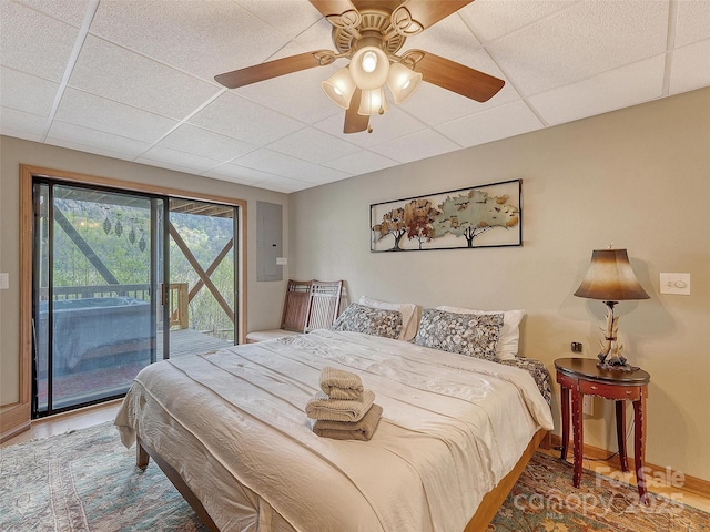 bedroom featuring a paneled ceiling, access to outside, electric panel, wood finished floors, and a ceiling fan