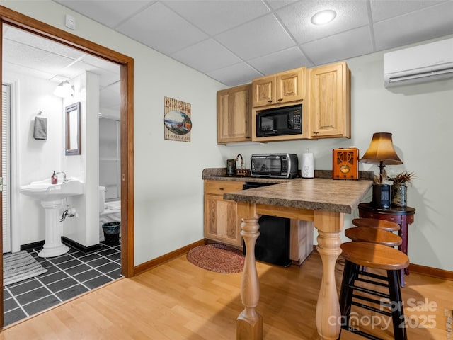 kitchen with a drop ceiling, dark countertops, black microwave, baseboards, and an AC wall unit
