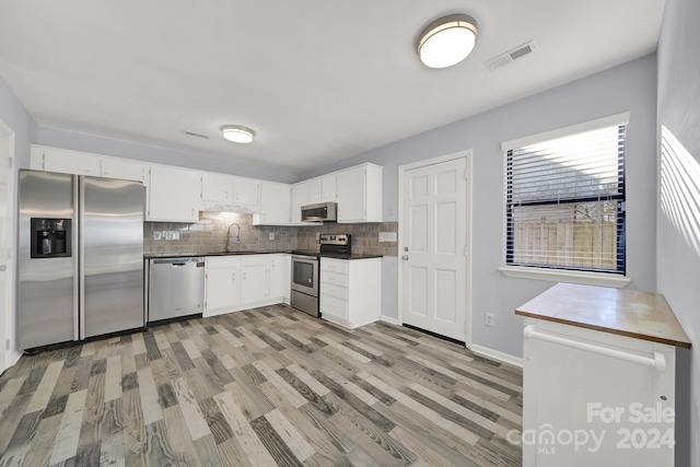 kitchen with backsplash, white cabinets, sink, light wood-type flooring, and appliances with stainless steel finishes