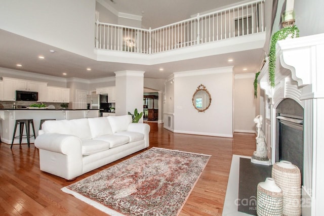 living room with crown molding, a towering ceiling, and light hardwood / wood-style flooring