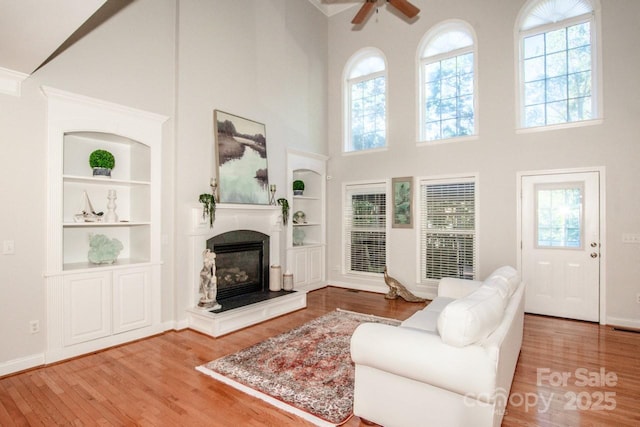 living room with a towering ceiling, built in features, hardwood / wood-style flooring, ceiling fan, and a premium fireplace