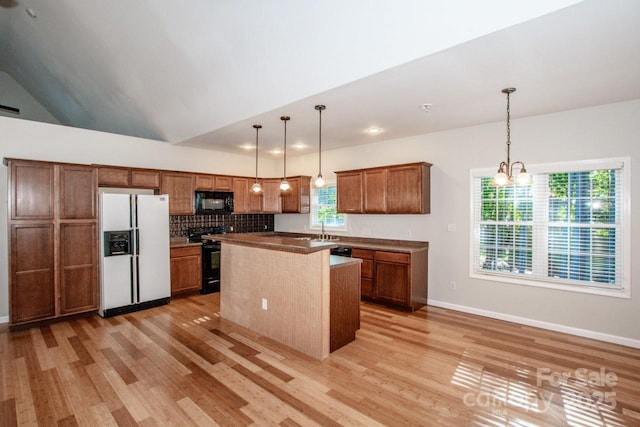 kitchen with an inviting chandelier, hanging light fixtures, black appliances, a kitchen island, and light wood-type flooring