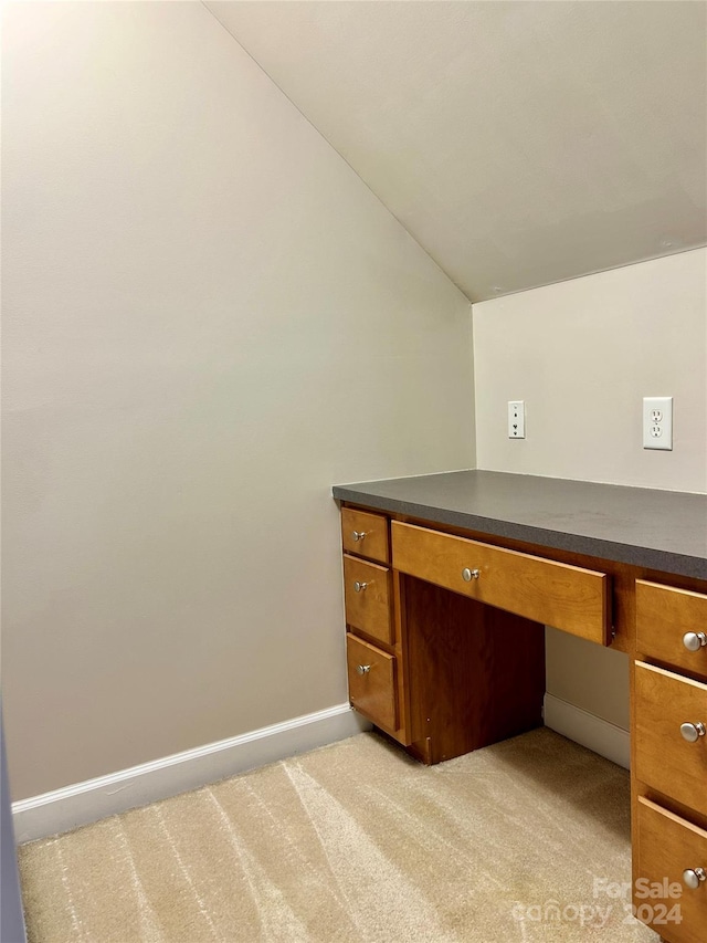 unfurnished office featuring light carpet, built in desk, and vaulted ceiling