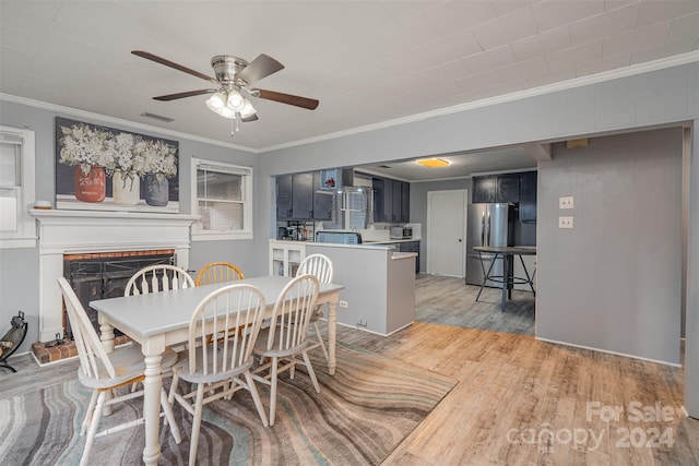 dining area with a brick fireplace, crown molding, ceiling fan, and light wood-type flooring