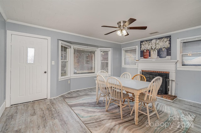 dining space with ceiling fan, light hardwood / wood-style flooring, ornamental molding, and a brick fireplace