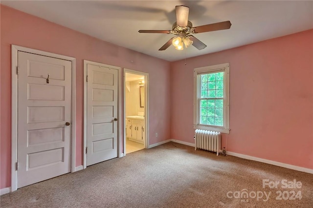 unfurnished bedroom featuring ceiling fan, radiator heating unit, ensuite bathroom, and light carpet